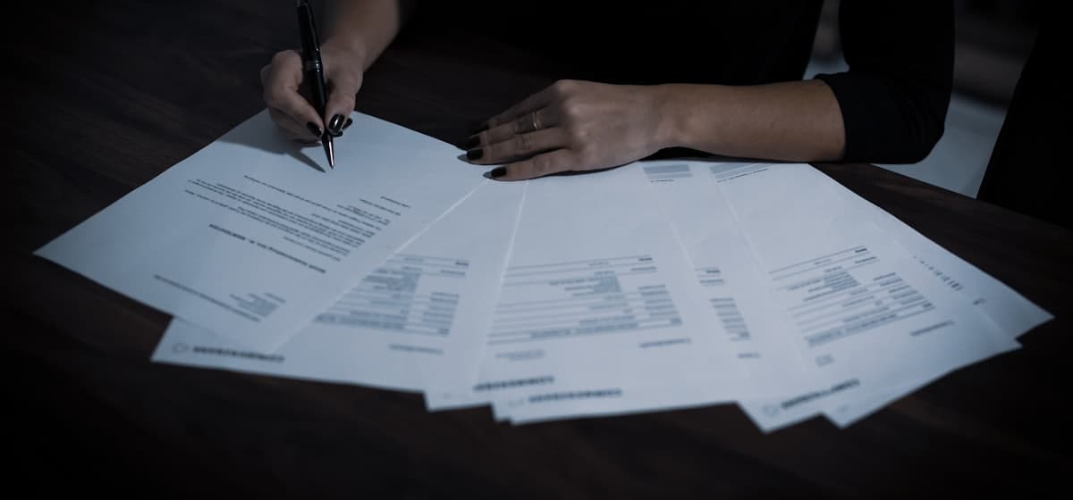 Someone working through a fan of printed application forms with a pen, one already signed.