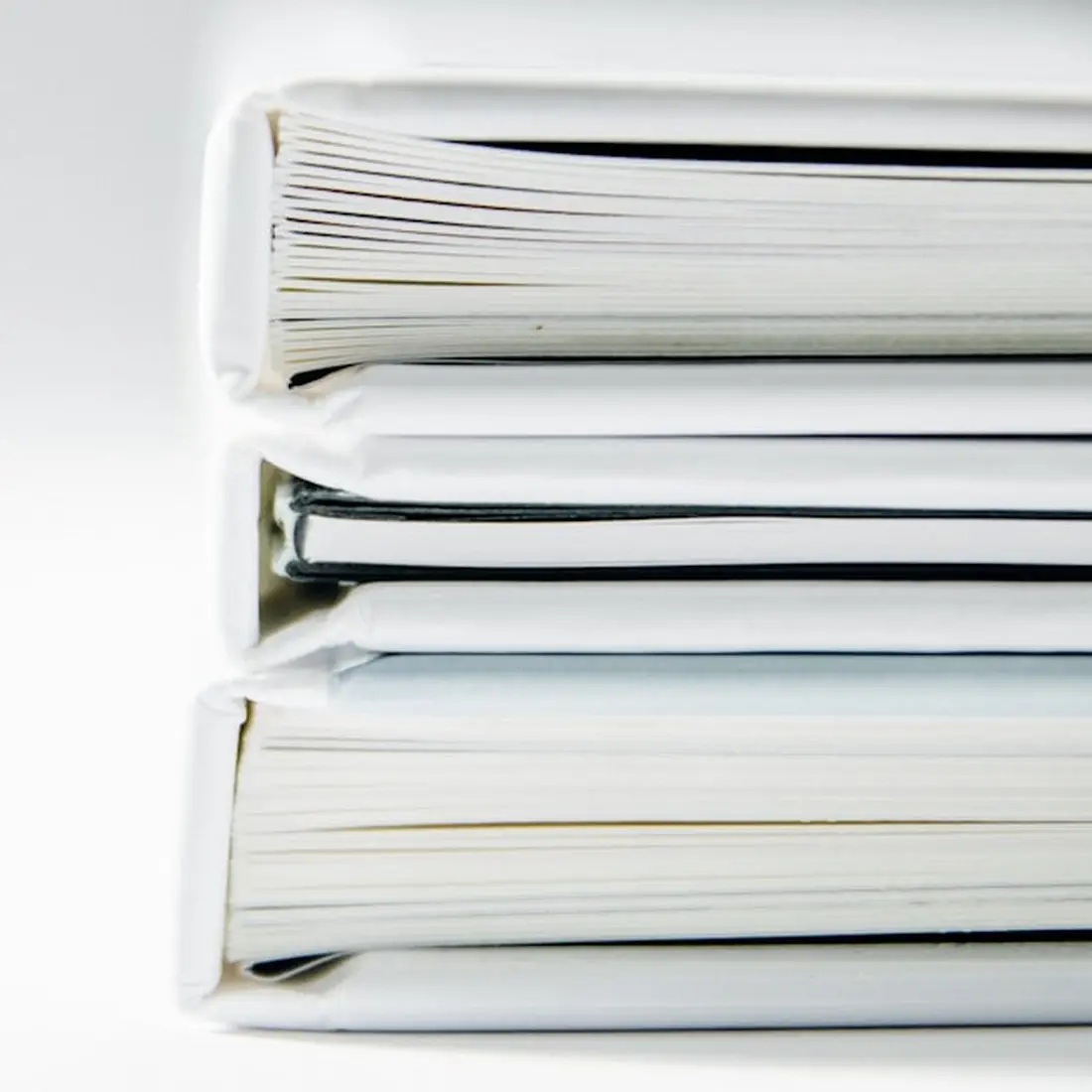 Three thick document files stacked on a white surface, their pages fanned at the edges.