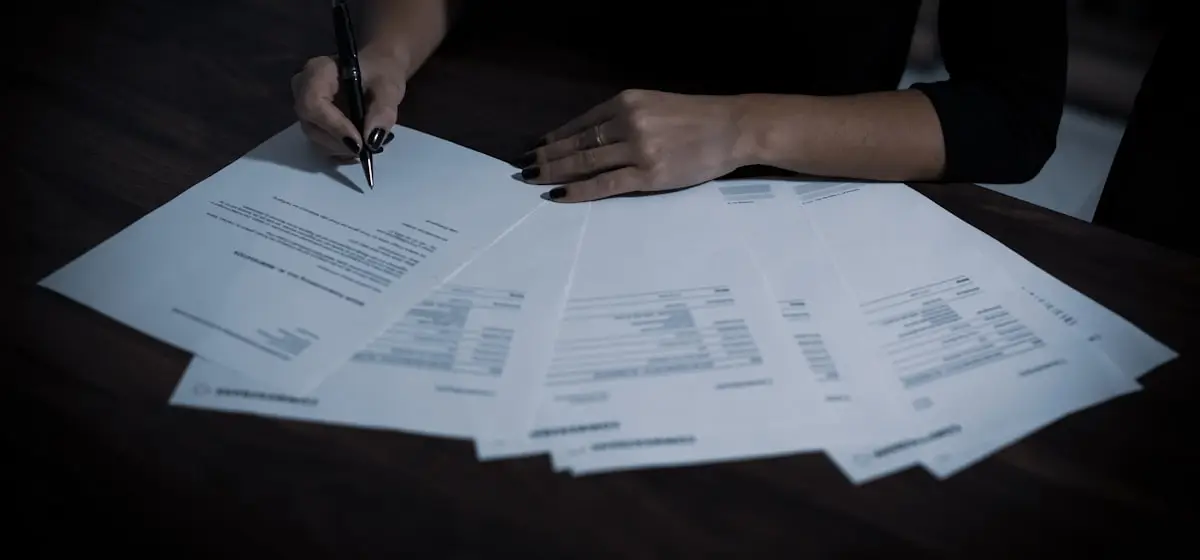 Someone working through a fan of printed application forms with a pen, one already signed.